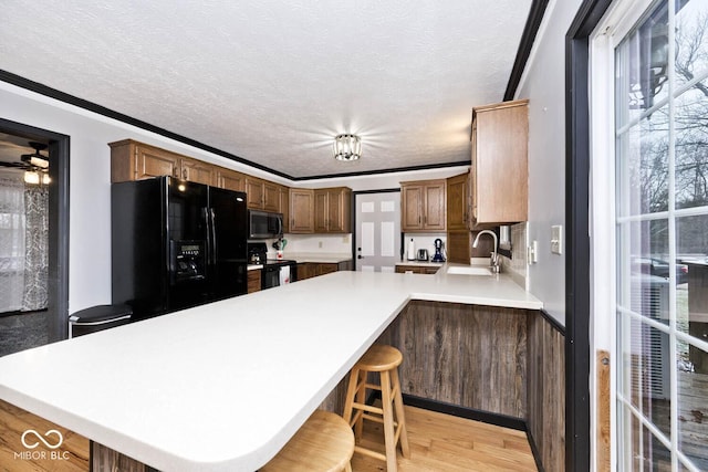 kitchen featuring kitchen peninsula, light wood-type flooring, a kitchen bar, black appliances, and ornamental molding