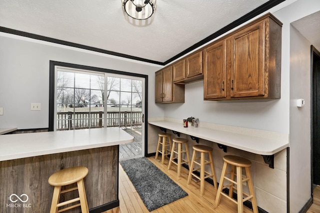 kitchen featuring light hardwood / wood-style floors, a kitchen bar, kitchen peninsula, and ornamental molding