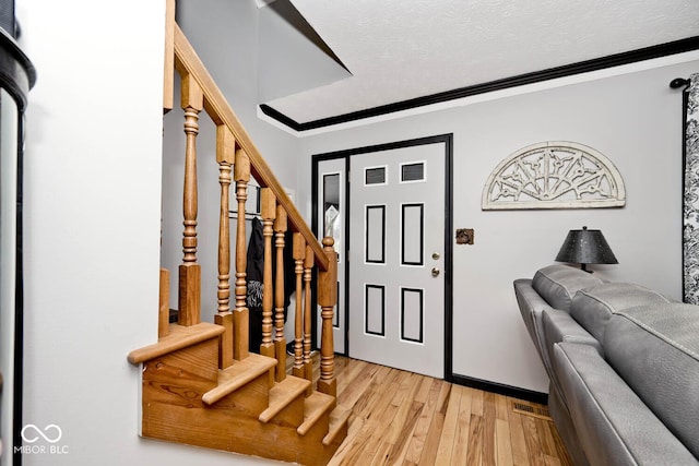 foyer with a textured ceiling, light wood-type flooring, and ornamental molding