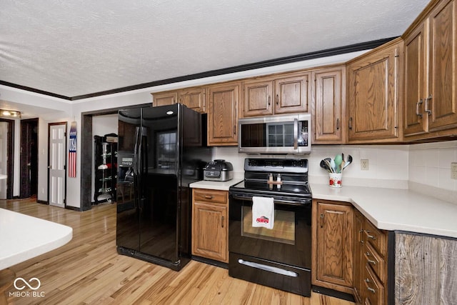 kitchen with a textured ceiling, light hardwood / wood-style flooring, ornamental molding, and black appliances