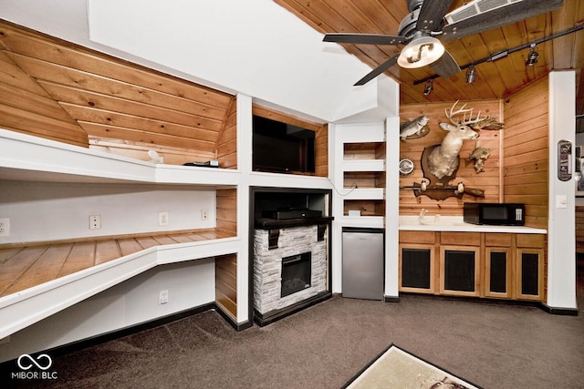 kitchen with ceiling fan, refrigerator, wooden walls, a fireplace, and dark carpet