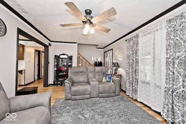 living room with crown molding, light hardwood / wood-style flooring, ceiling fan, and a textured ceiling