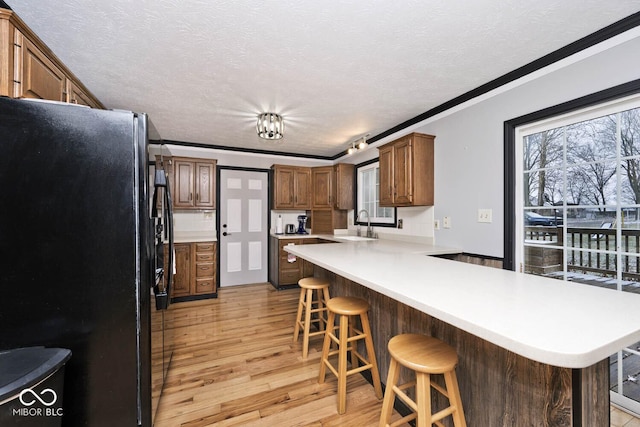 kitchen with black refrigerator, kitchen peninsula, a breakfast bar, crown molding, and light hardwood / wood-style floors