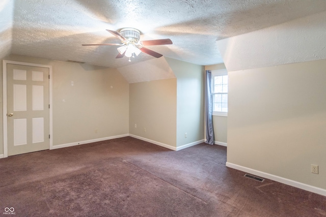 additional living space with a textured ceiling, lofted ceiling, dark carpet, and ceiling fan