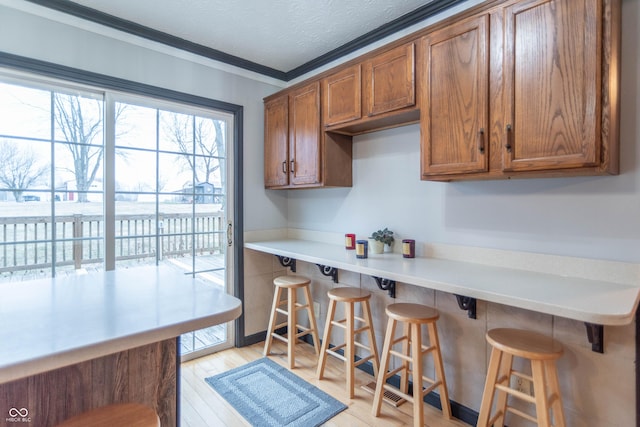 kitchen featuring crown molding, a breakfast bar, a textured ceiling, and light wood-type flooring