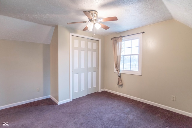 interior space with a closet, a textured ceiling, ceiling fan, dark colored carpet, and vaulted ceiling