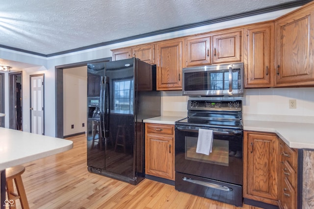 kitchen with light wood-type flooring, a textured ceiling, crown molding, black appliances, and decorative backsplash