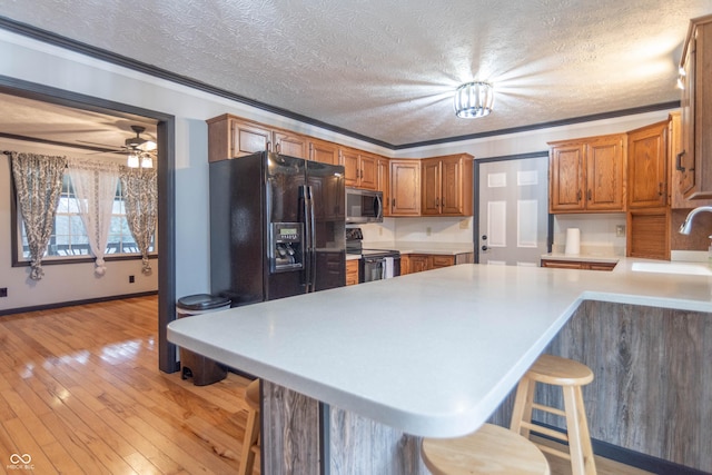 kitchen with a kitchen bar, sink, light wood-type flooring, black appliances, and kitchen peninsula