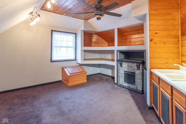 additional living space featuring lofted ceiling, ceiling fan, dark colored carpet, a fireplace, and sink