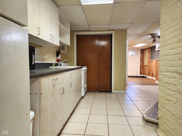 kitchen with a drop ceiling, wood walls, sink, ceiling fan, and light tile patterned flooring