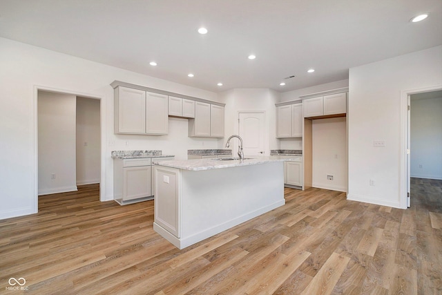 kitchen with a center island with sink, light stone counters, light wood-type flooring, and sink