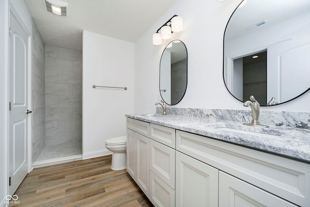 bathroom with hardwood / wood-style flooring, vanity, toilet, and tiled shower