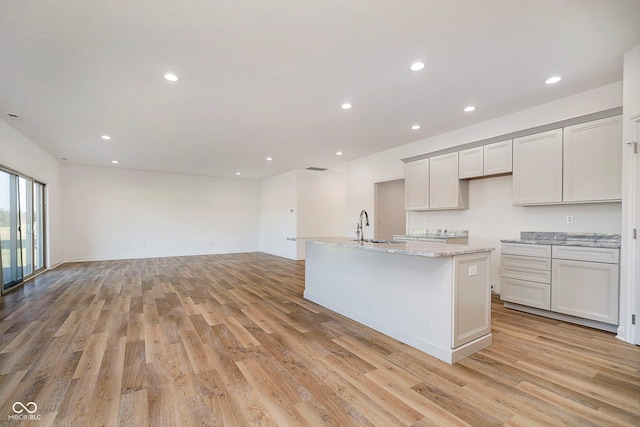 kitchen featuring light stone counters, sink, light hardwood / wood-style flooring, white cabinets, and an island with sink