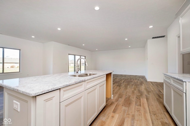 kitchen with light stone countertops, sink, a center island with sink, white cabinets, and light hardwood / wood-style floors