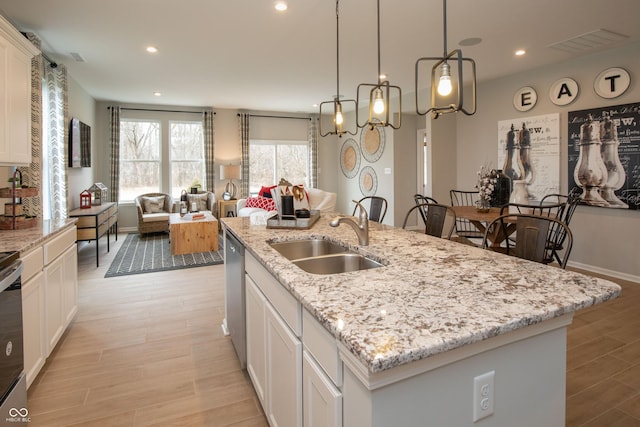 kitchen with a kitchen island with sink, sink, white cabinets, and light hardwood / wood-style floors