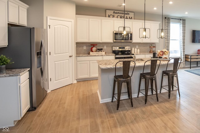 kitchen featuring a kitchen island with sink, white cabinetry, stainless steel appliances, and hanging light fixtures