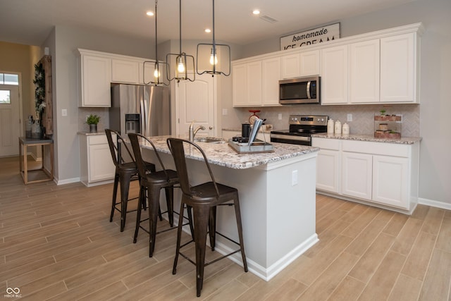 kitchen with white cabinets, sink, an island with sink, appliances with stainless steel finishes, and a breakfast bar area