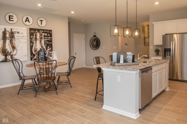 kitchen with white cabinetry, stainless steel appliances, a kitchen island with sink, and light hardwood / wood-style flooring