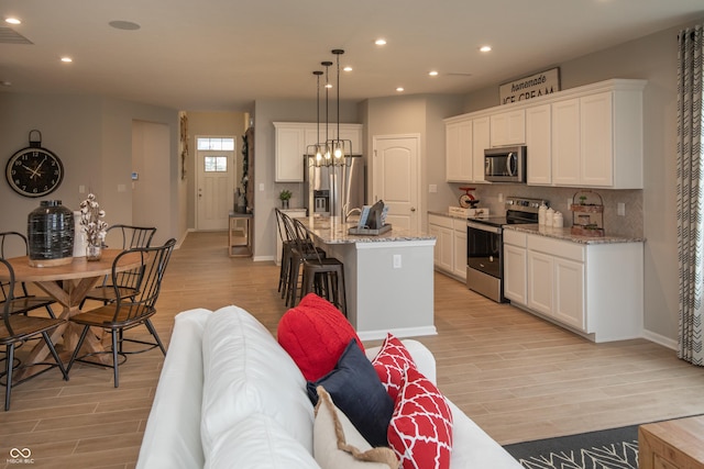 kitchen with white cabinetry, light stone counters, an island with sink, pendant lighting, and appliances with stainless steel finishes