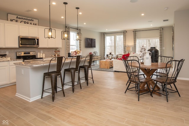 kitchen with pendant lighting, a center island with sink, a kitchen breakfast bar, appliances with stainless steel finishes, and light hardwood / wood-style floors