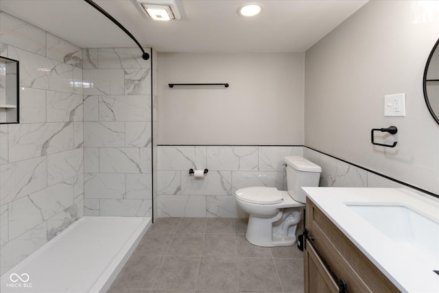 bathroom featuring a tile shower, tile patterned flooring, toilet, vanity, and tile walls