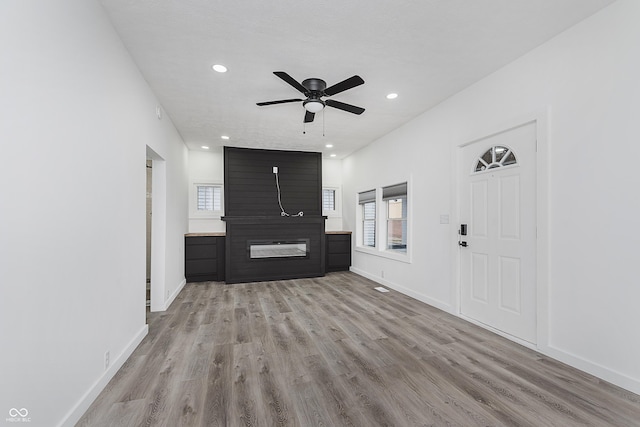 unfurnished living room with a textured ceiling, a large fireplace, light hardwood / wood-style flooring, and ceiling fan