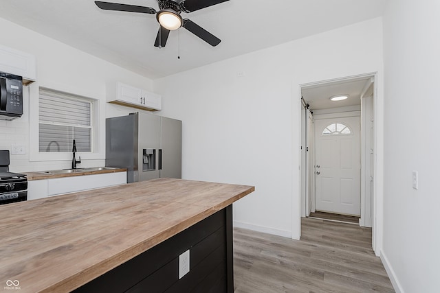 kitchen featuring black appliances, white cabinets, sink, light wood-type flooring, and butcher block counters