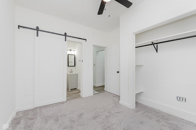 unfurnished bedroom with ensuite bath, light colored carpet, ceiling fan, a barn door, and a closet