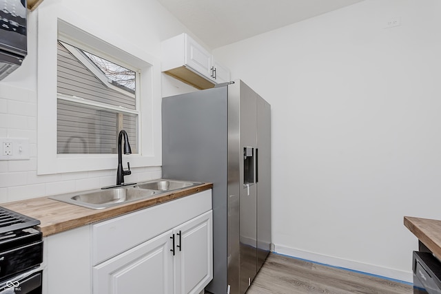 kitchen with white cabinetry, sink, wooden counters, stainless steel refrigerator with ice dispenser, and light wood-type flooring