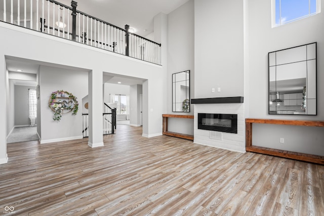 unfurnished living room featuring light hardwood / wood-style floors, plenty of natural light, and a towering ceiling