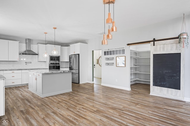 kitchen featuring appliances with stainless steel finishes, wall chimney range hood, a kitchen island, white cabinets, and pendant lighting