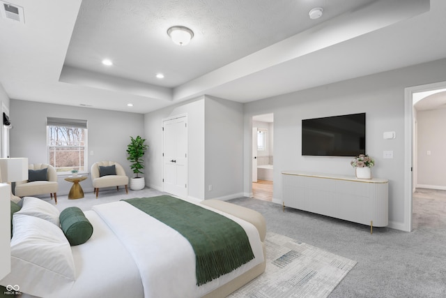 bedroom with light carpet, a textured ceiling, ensuite bathroom, and a raised ceiling