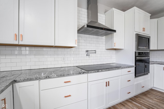 kitchen featuring built in microwave, wall oven, black electric stovetop, white cabinetry, and wall chimney exhaust hood