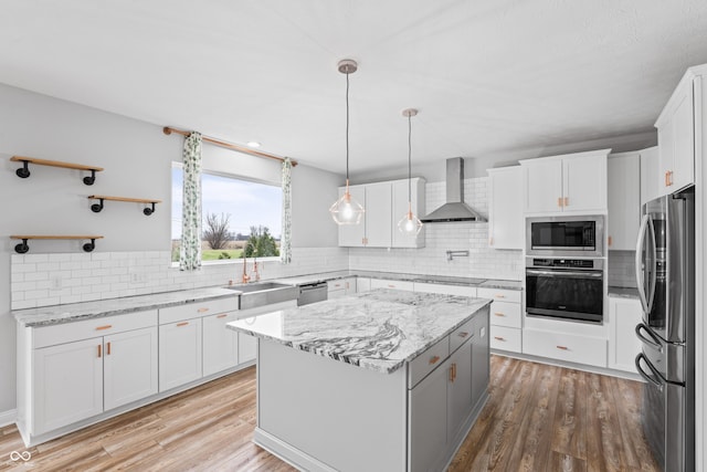 kitchen featuring appliances with stainless steel finishes, decorative light fixtures, white cabinetry, a center island, and wall chimney range hood