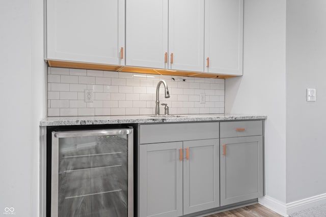 bar with sink, backsplash, light stone countertops, and beverage cooler