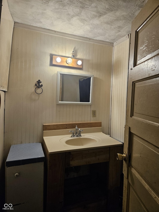 bathroom featuring a textured ceiling, vanity, and wooden walls