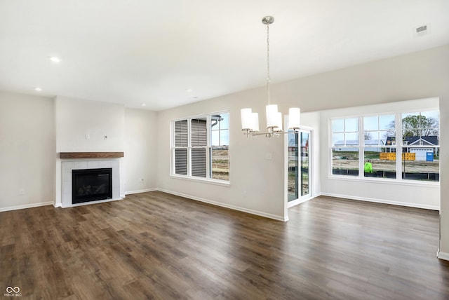 unfurnished living room featuring plenty of natural light, dark wood-type flooring, a tile fireplace, and an inviting chandelier