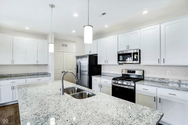 kitchen featuring white cabinetry, sink, decorative light fixtures, a kitchen island with sink, and appliances with stainless steel finishes