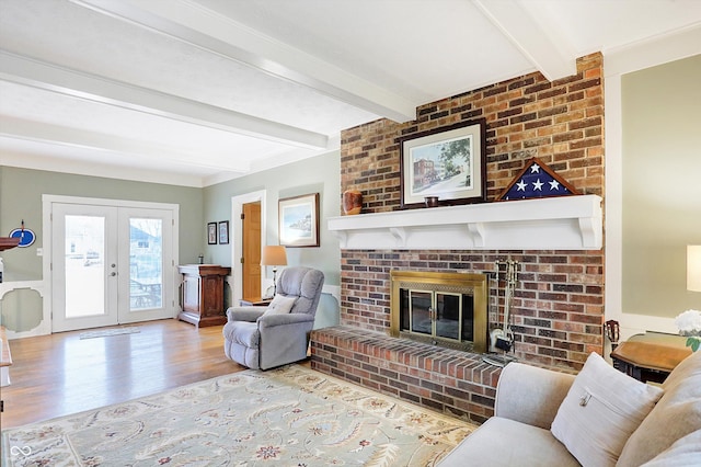 living room featuring beam ceiling, light wood-type flooring, french doors, and a brick fireplace