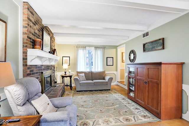 living room with beam ceiling, light hardwood / wood-style flooring, and a brick fireplace