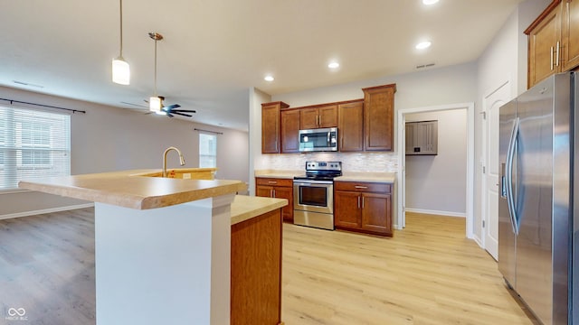 kitchen with sink, hanging light fixtures, stainless steel appliances, tasteful backsplash, and light wood-type flooring