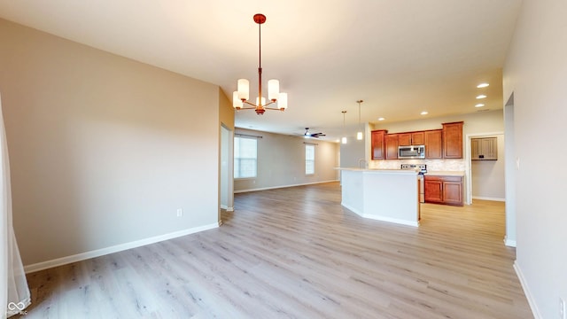 kitchen featuring appliances with stainless steel finishes, decorative light fixtures, decorative backsplash, a kitchen island, and light wood-type flooring