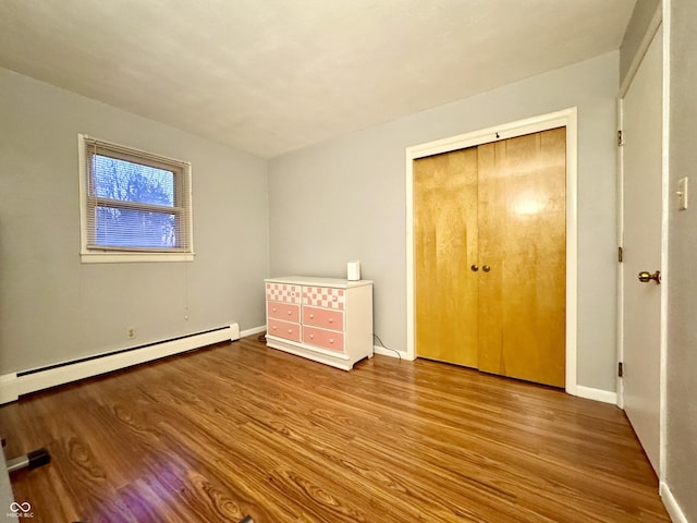 unfurnished bedroom featuring baseboard heating, a closet, and hardwood / wood-style floors