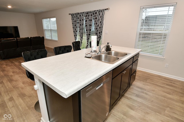 kitchen with light wood-type flooring, stainless steel dishwasher, a kitchen island with sink, and sink