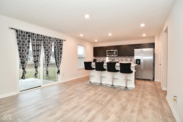 kitchen featuring a center island, a kitchen breakfast bar, backsplash, appliances with stainless steel finishes, and light wood-type flooring