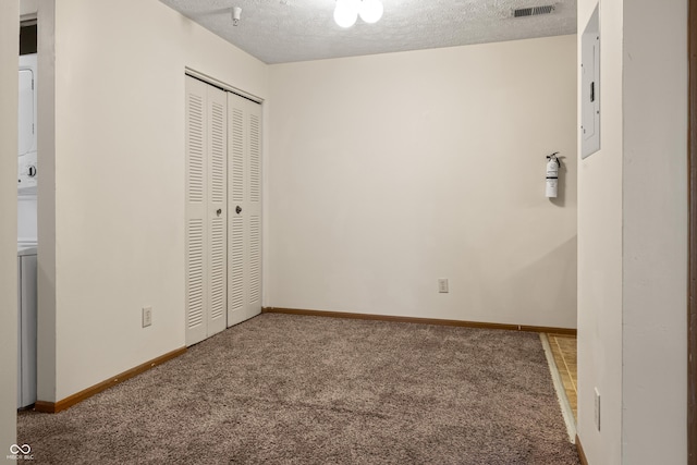 unfurnished bedroom featuring carpet, electric panel, stacked washer and dryer, a textured ceiling, and a closet