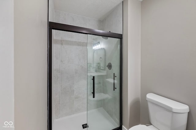 bathroom with a textured ceiling, an enclosed shower, and toilet