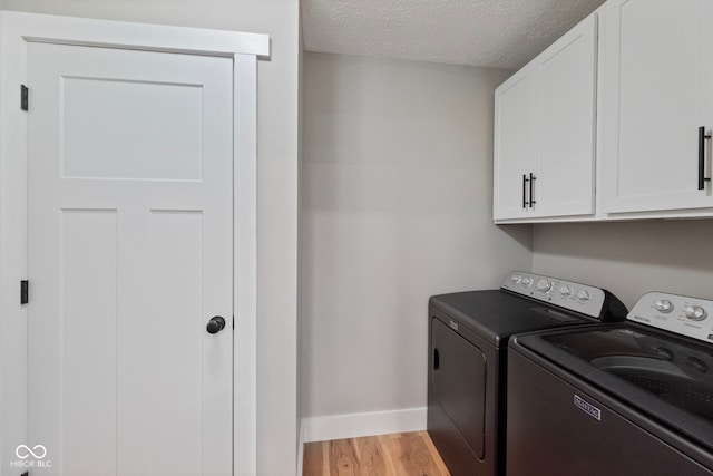 clothes washing area with separate washer and dryer, light hardwood / wood-style flooring, cabinets, and a textured ceiling