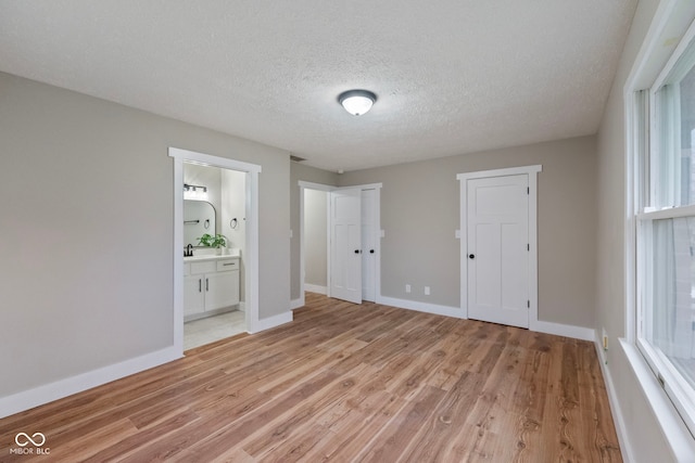 unfurnished bedroom featuring ensuite bath, light hardwood / wood-style flooring, and a textured ceiling