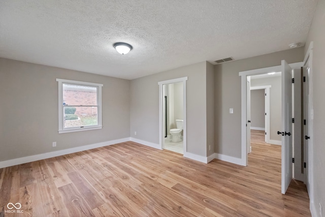 unfurnished bedroom with ensuite bath, a textured ceiling, and light wood-type flooring